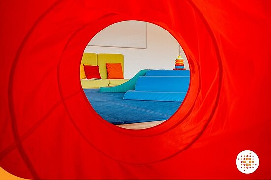 Foto: roter Hintergrund mit Liegewiese und Kinderspielzeug