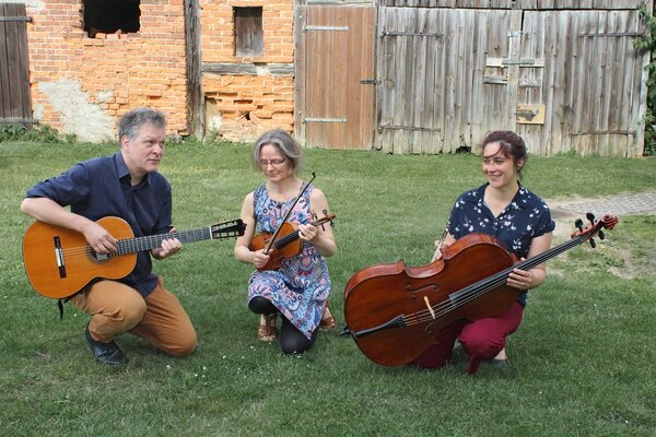 Foto: 3 Musiker mit Saiteninstrumenten vor einem alten Gebäude