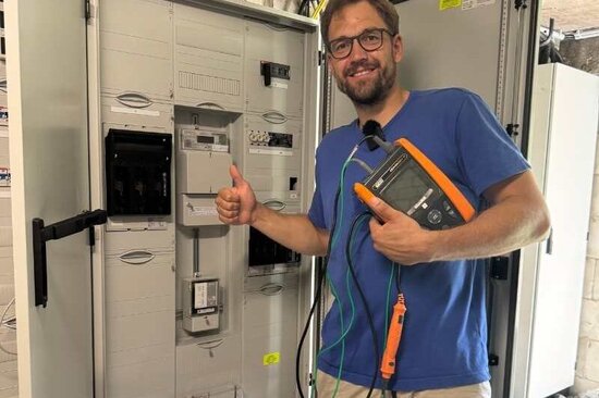 Elektriker vor einem Sicherungskasten mit Messgerät in der Hand