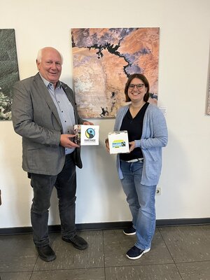 Foto: Meinolf Thiemann und Linda Sauer vor einem Gemälde mit Broschüren in der Hand