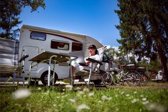 Foto: Wohnmobil mit einer Person im Campingstühl davor 