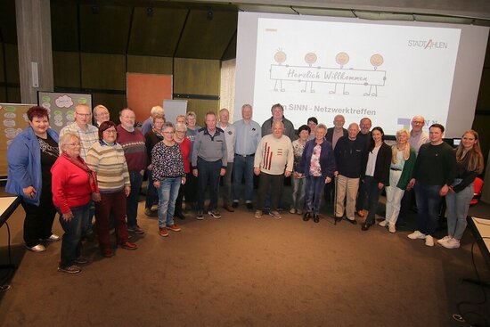 Foto. Menschengruppe vor einer Leinwand mit "Herzliche Willkommen -  SINN-Netzwerktreffen"