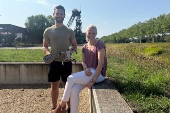 Mann und Frau mit Drohne in der Hand, Blick zur Kamera, draußen vor Förderturm